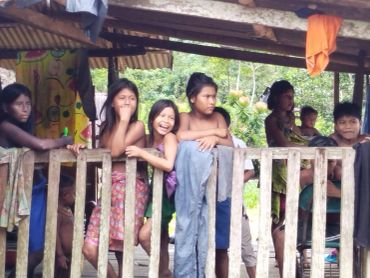 Children standing behind a wooden fence in a rural setting.