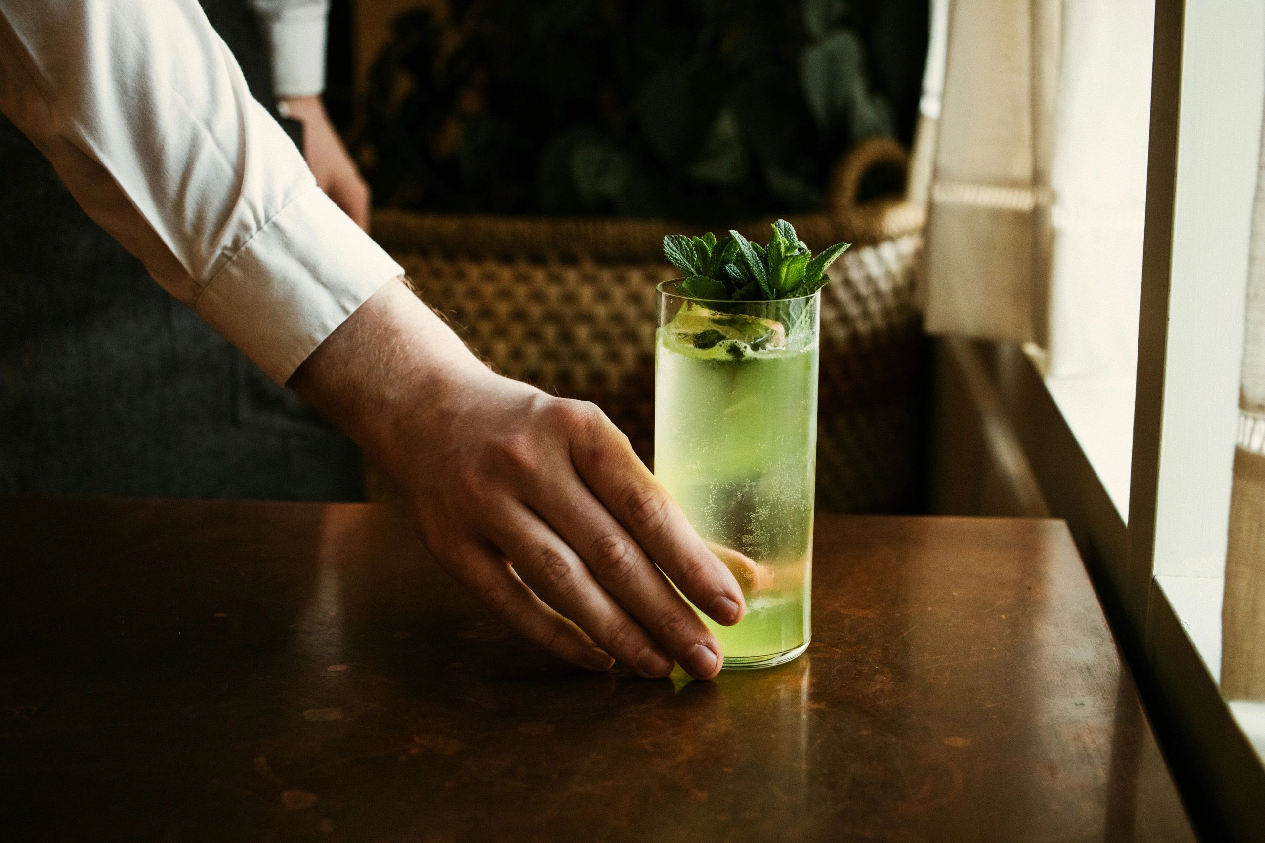 Hand placing a refreshing green mint drink on a wooden table.