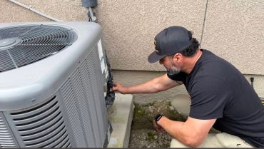Technician inspecting an air conditioning unit outdoors.