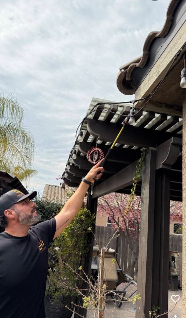 Man adjusting outdoor string lights on patio cover.