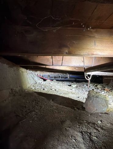 Dimly lit crawl space with dirt floor and wooden beams.