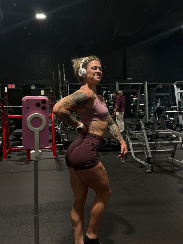 A fit woman posing confidently in gym attire with headphones on.