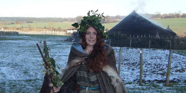 Terrie Howey-Moore in iron age costume crowned with holly and ivy, surrounded by snow with a round h
