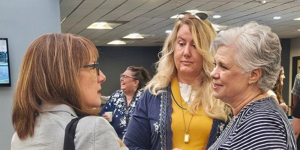 Three women engaged in a conversation indoors.
