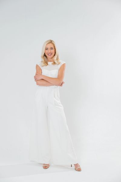 Smiling woman in white jumpsuit standing confidently with arms crossed.
