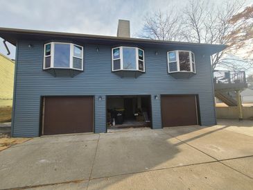 Blue house with three garage doors and bay windows above.