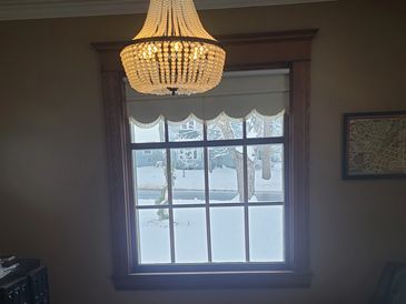 A window with wooden trim and a chandelier above, showing a snowy outdoor scene.