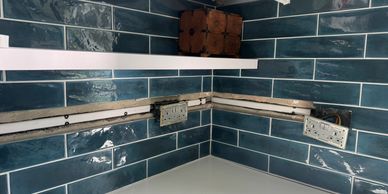 Kitchen backsplash with blue tiles and some exposed outlets.