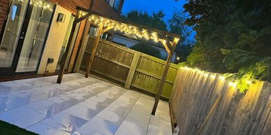 Cozy backyard patio with string lights under a wooden pergola at dusk.