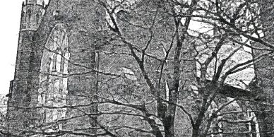 Black and white image of a gothic-style building behind leafless trees.