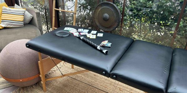 A black massage table with tarot cards and a flute on it, set in a cozy, plant-filled room.