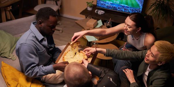 Friends sharing pizza while watching a soccer game on TV.