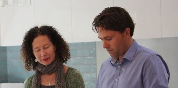 Two people reviewing blueprints on a wooden table in a kitchen.