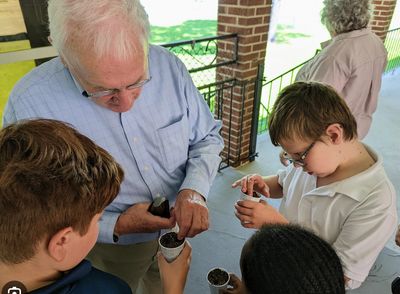 Older man teaching kids how to plant seeds in cups outdoors.