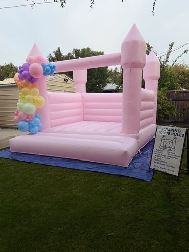 Pink inflatable bounce house decorated with colorful balloons in a backyard.