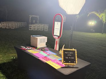 Outdoor photo booth setup at night with bright lighting and colorful props on a table.