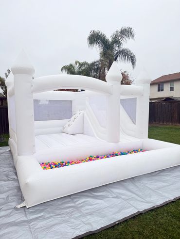 White inflatable bounce house with colorful ball pit outside on a lawn.