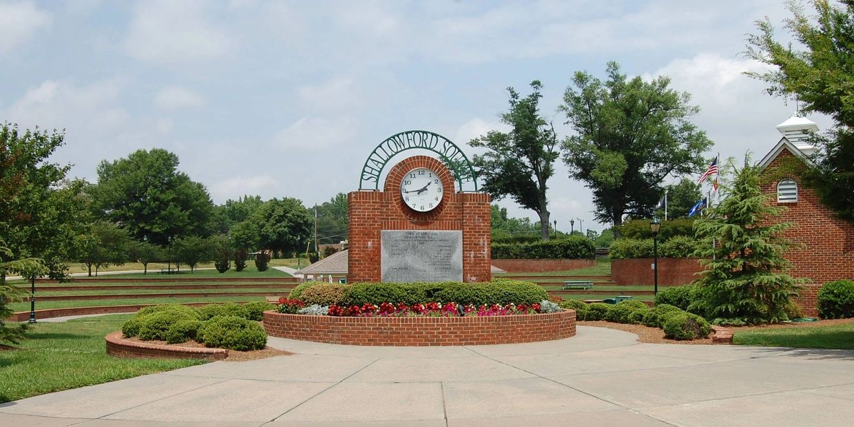 Brick clock monument with 'Shallowford Square' sign in a park.