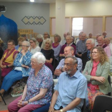 A group of elderly people seated and attentively listening indoors.