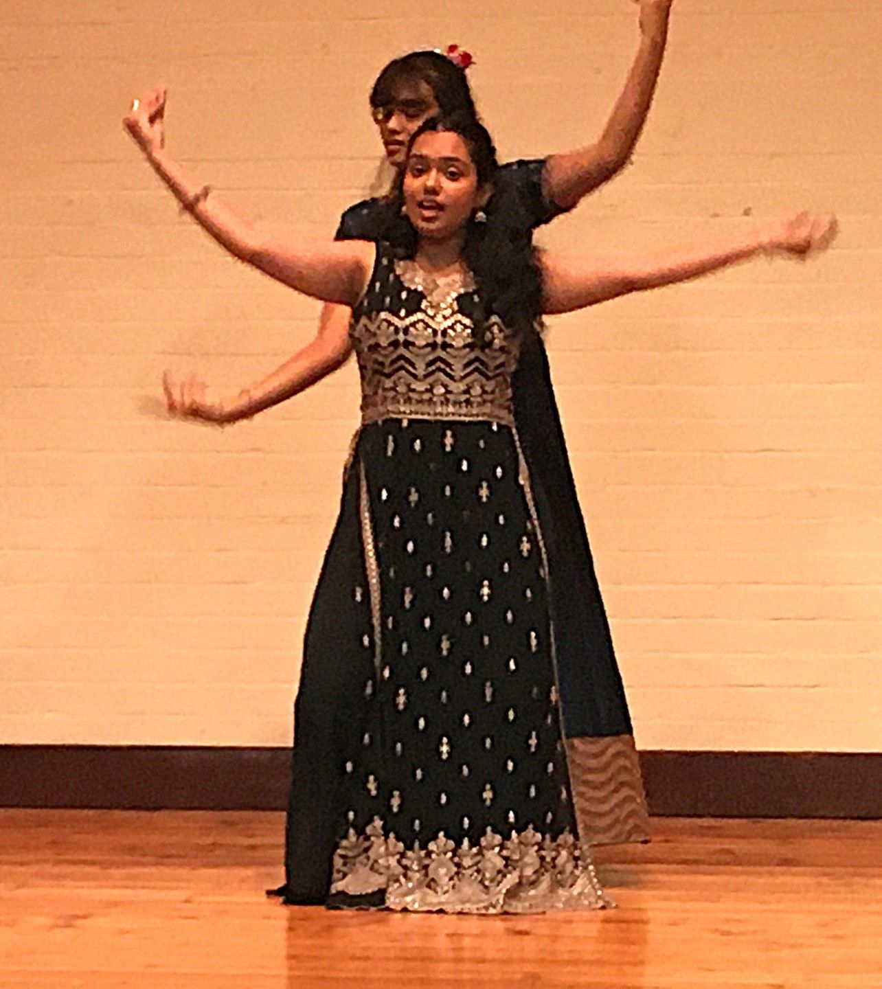 Two women performing a traditional dance on stage in elegant black and gold outfits.