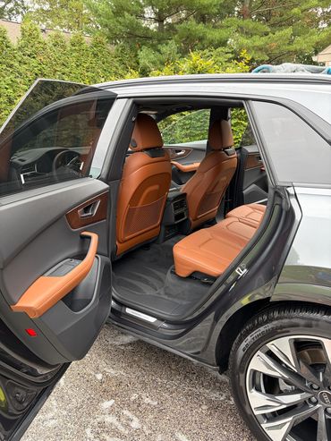 Open rear door revealing luxurious tan leather seats and modern car interior.
