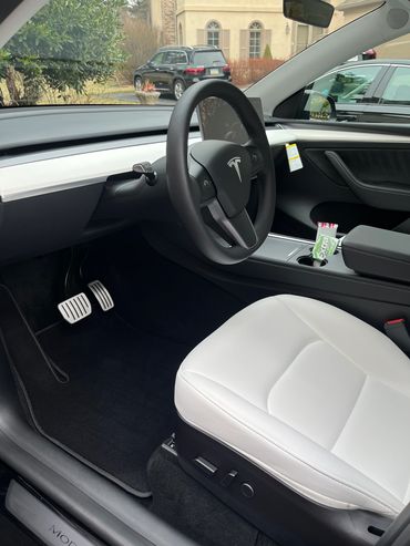 Interior of a Tesla Model 3 with white seats and a sleek steering wheel.