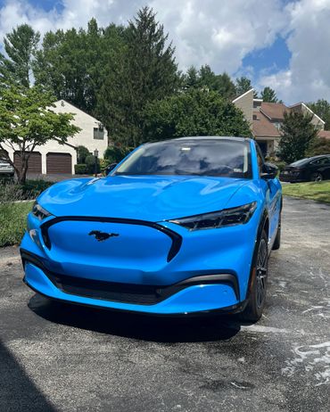 Bright blue Ford Mustang electric car in a residential driveway.