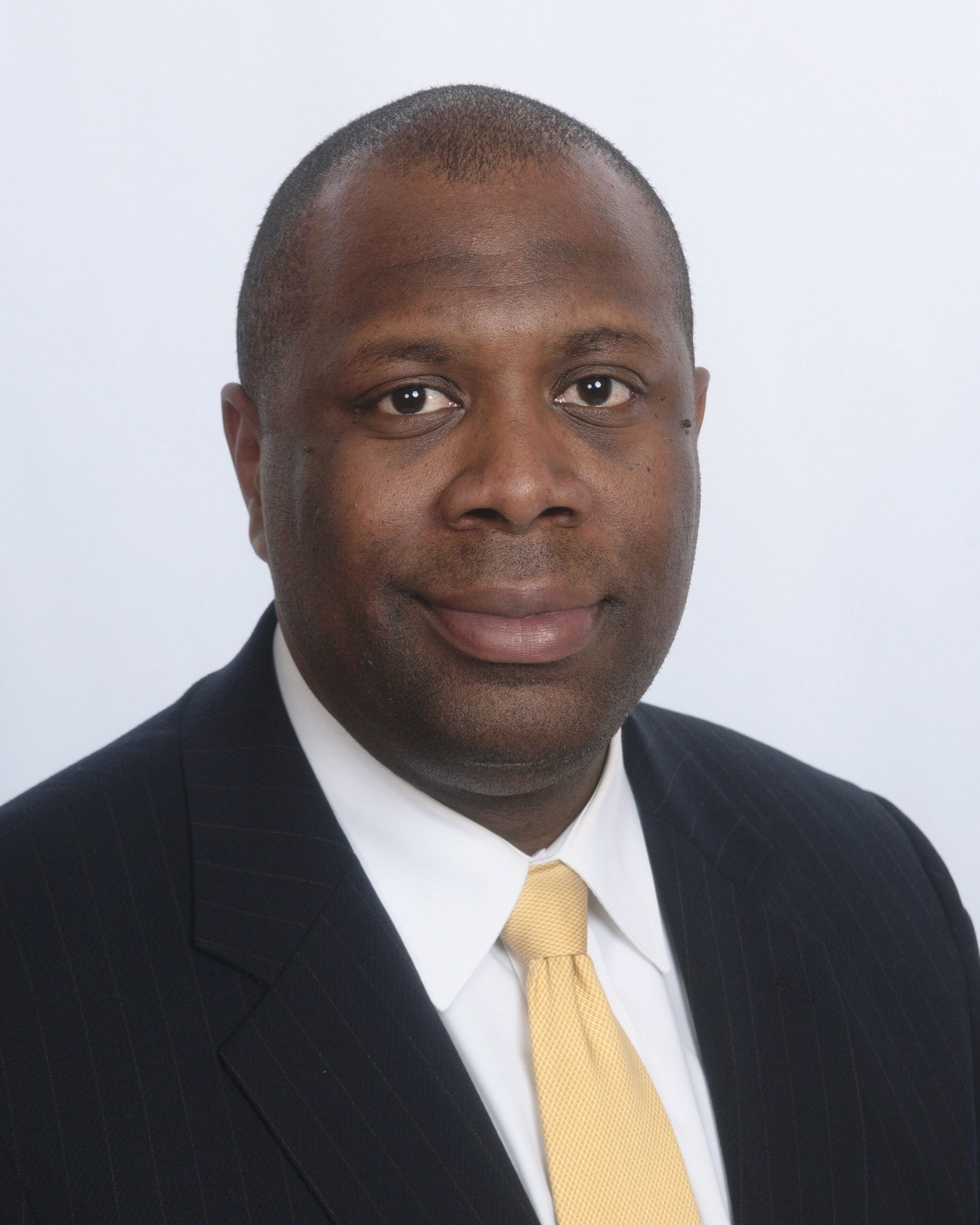 Professional portrait of a man in a suit and yellow tie.