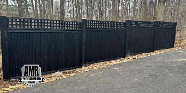 Black wooden fence with lattice top along a wooded area.