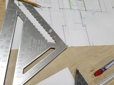 A tabletop is covered with building plans, pencils and drawings tools