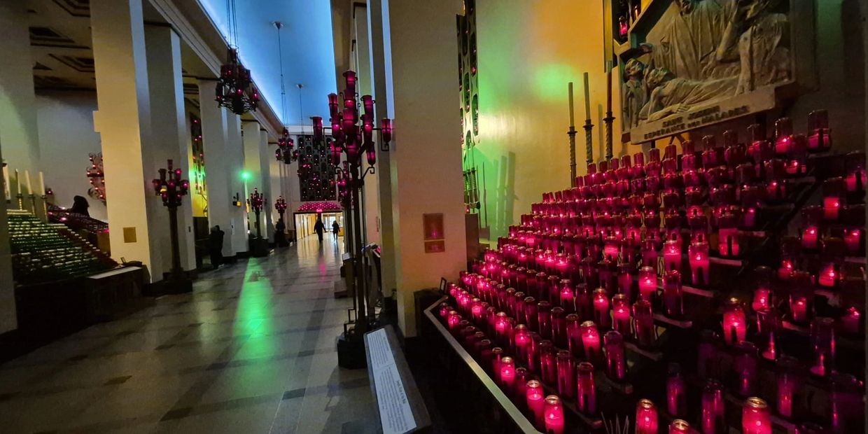 Dimly lit church interior with rows of red prayer candles and glowing chandeliers.