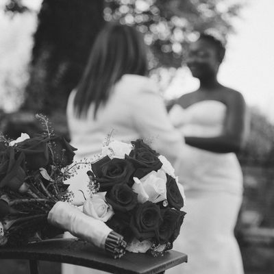 Black and white photo of a wedding bouquet with a bride and another woman in the background.