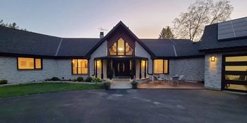 Modern stone house with large windows and warm lighting at dusk.