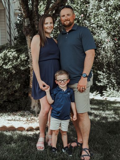A family of three posing outdoors, smiling warmly.