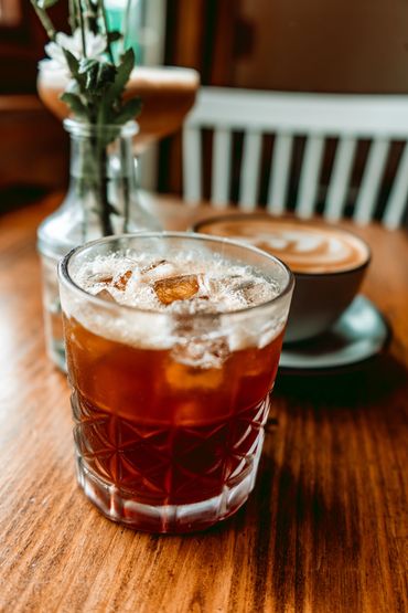 Iced coffee in a glass with a latte in the background on a wooden table.