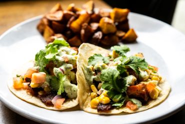 Two tacos with fresh toppings and a side of roasted potatoes on a white plate.