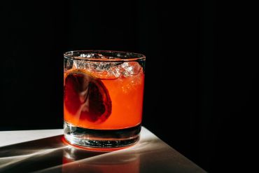 A vibrant orange cocktail with ice and a blood orange slice in a glass.