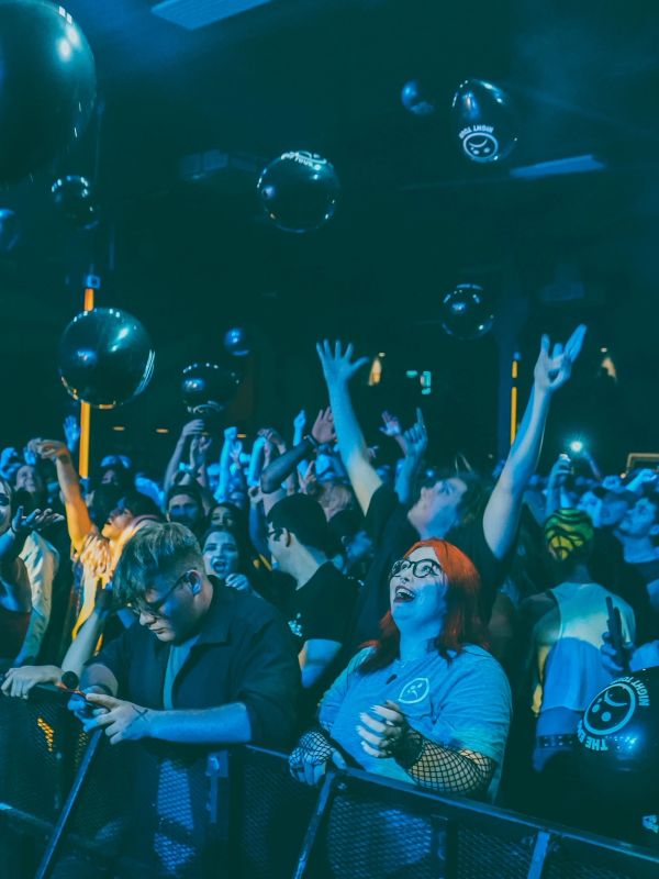 Excited crowd at a concert with black balloons floating above.