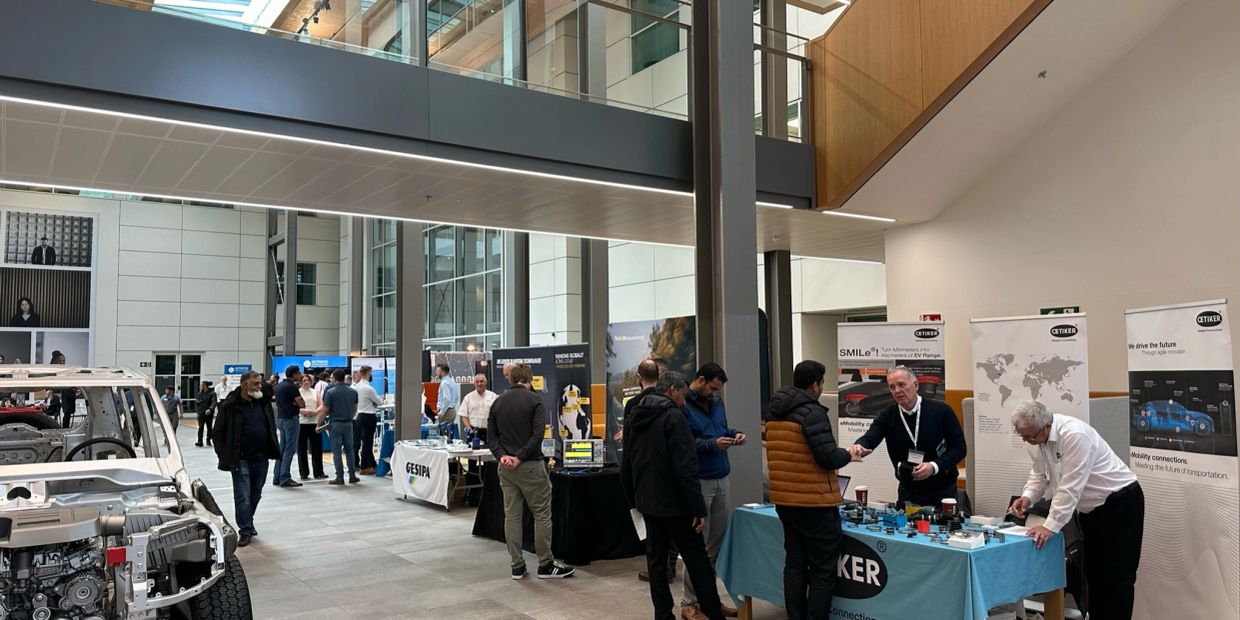 An indoor exhibition with people exploring automotive and technology booths.