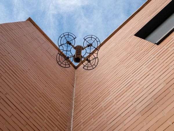 A drone flying between two brick walls with a blue sky background.