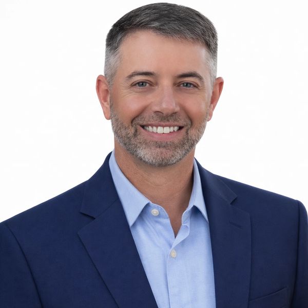 Smiling man in a blue suit and light blue shirt against a white background.