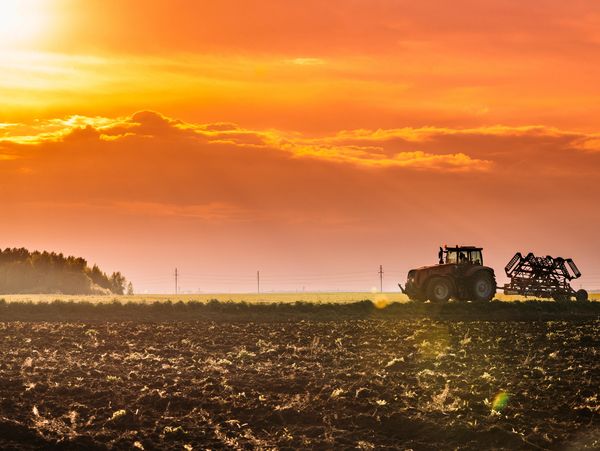 Tractor working on a field during a vibrant orange sunset.