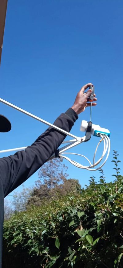 Person using a screwdriver to adjust an outdoor device under clear blue sky.