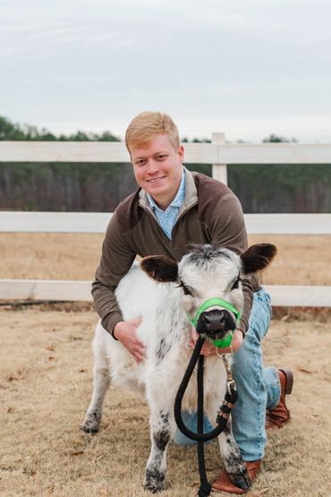 Young man kneeling with a small calf on a farm.