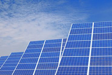 Rows of solar panels on green grass under a partly cloudy sky.