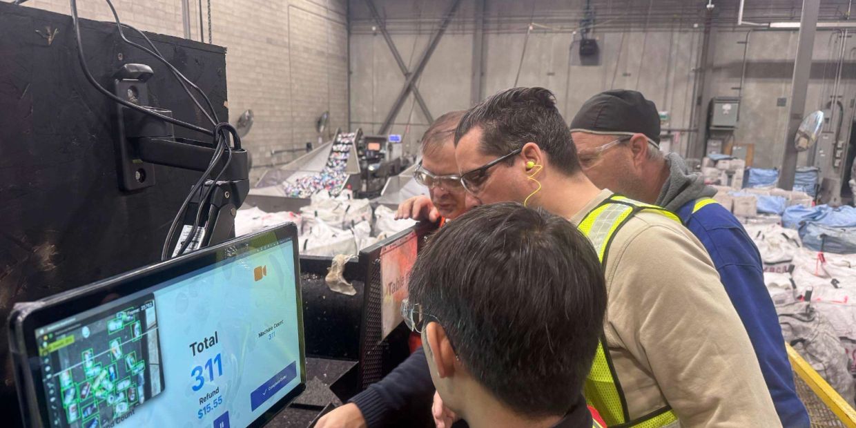 Workers monitoring a machine screen in an industrial setting.