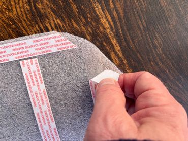 A hand peeling a protective adhesive strip on a textured surface.