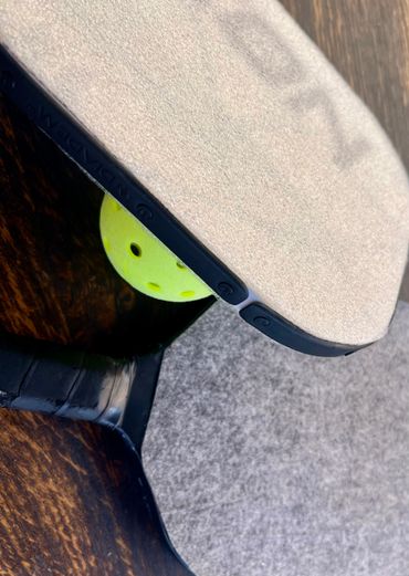 Close-up of pickleball paddles and a yellow pickleball ball on a wooden surface.