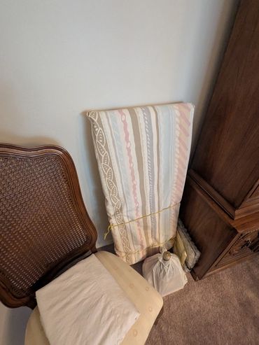 A chair with a cushion and folded items next to a wooden cabinet.