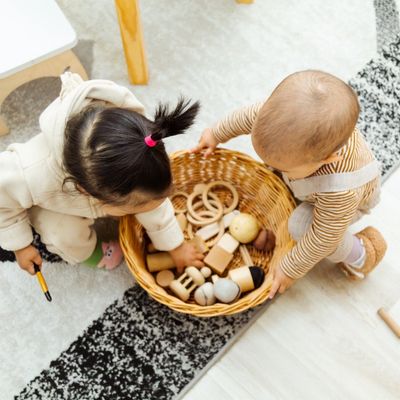 Two toddlers playing with wooden toys from a basket on the floor.